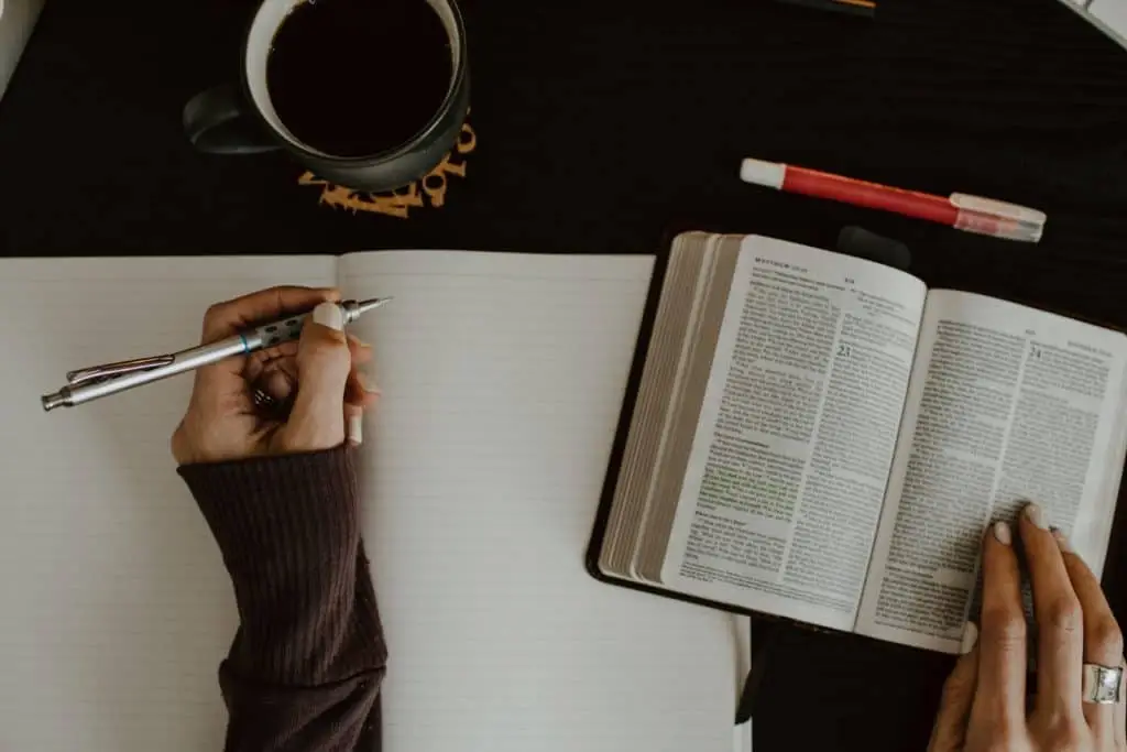 overhead shot of woman studying bible with notebook and pen