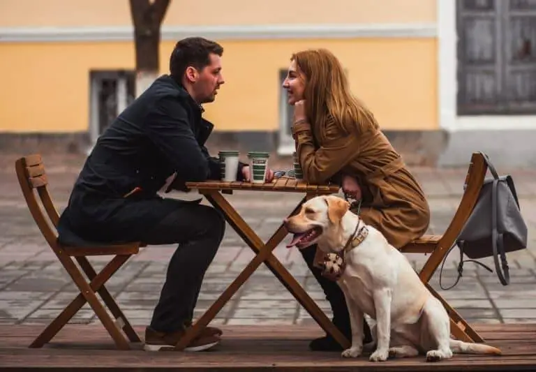 man and woman having coffee outside while dog is sitting next to woman