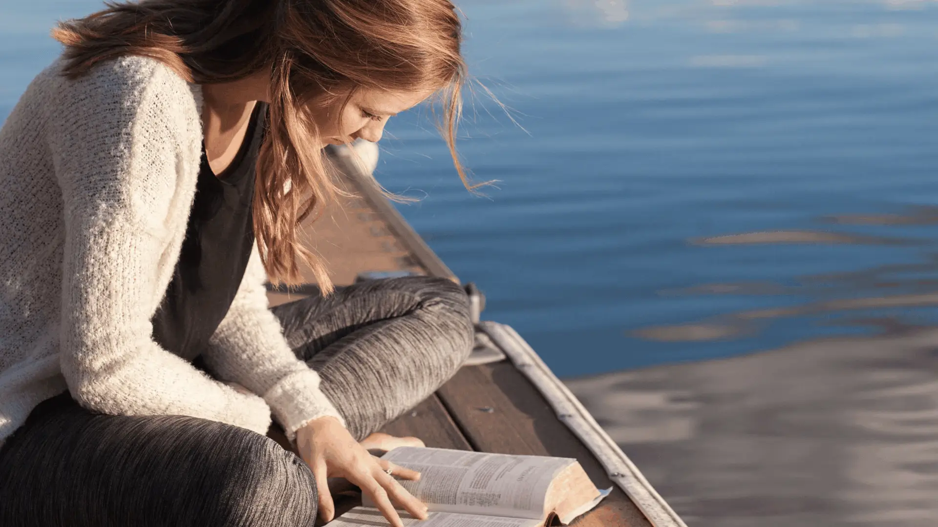 woman reading bible on lake dock