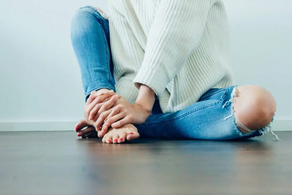 woman sitting on ground wearing white sweater and ripped jeans