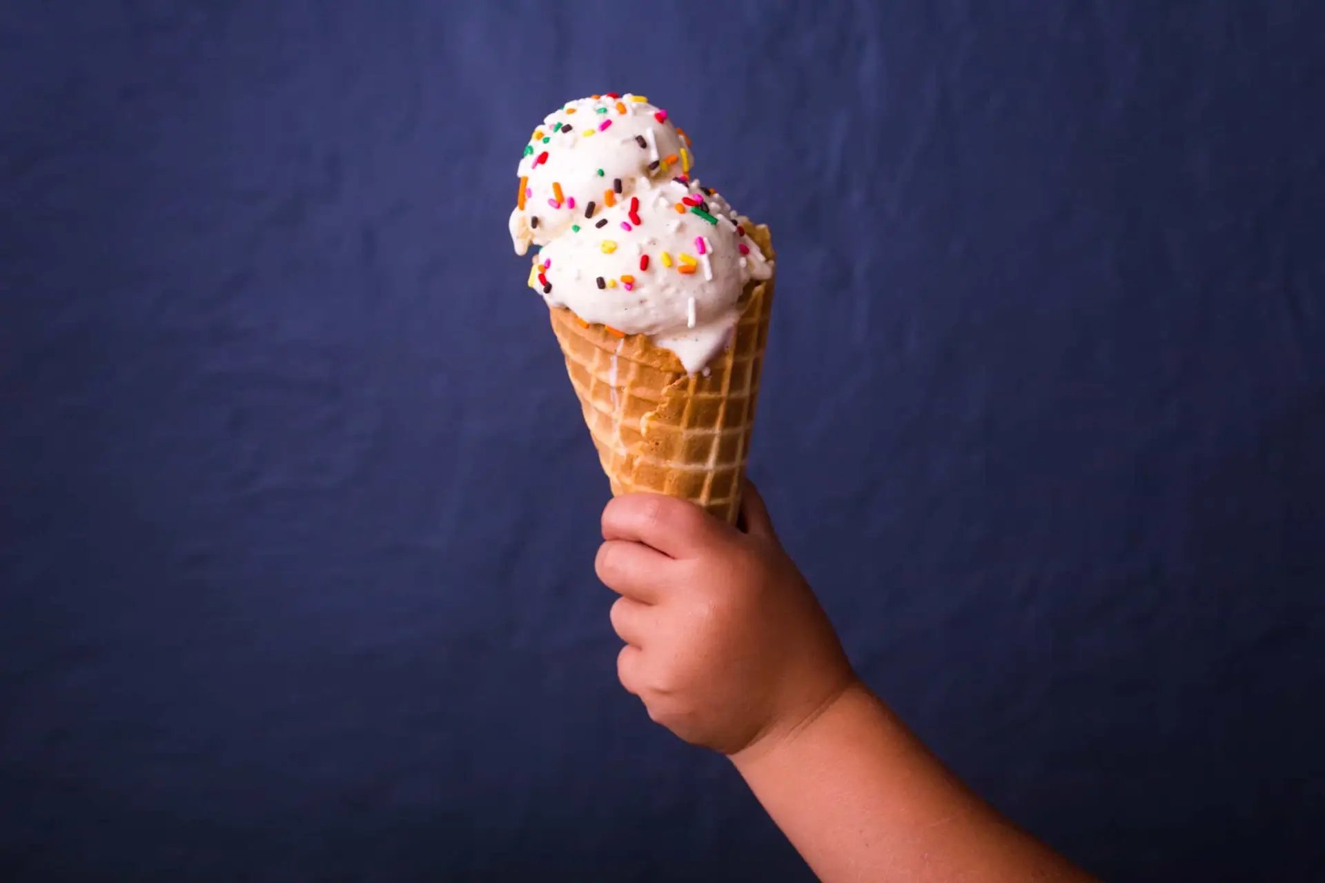 child holding ice cream cone in front of navy wall