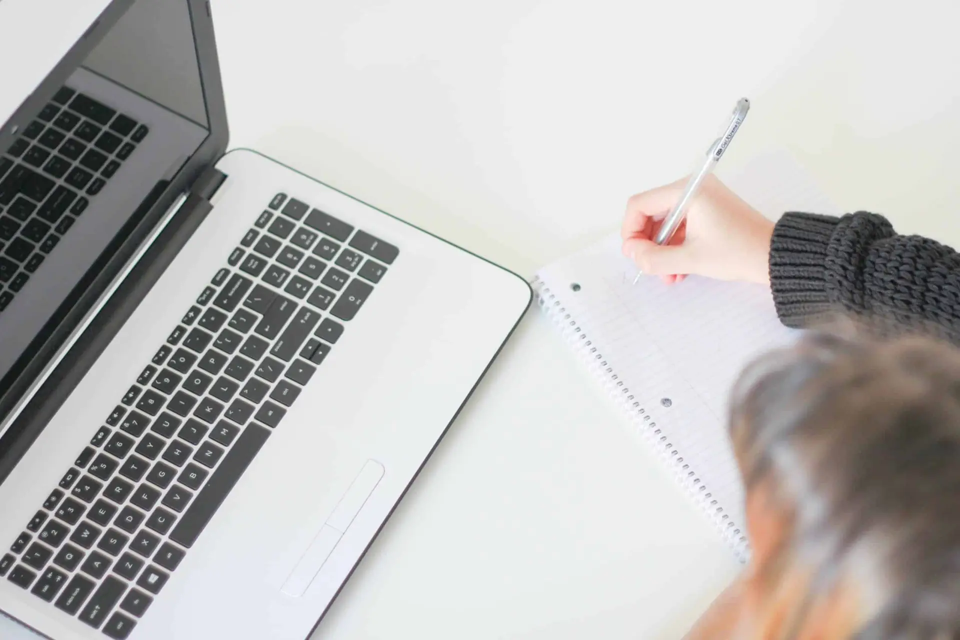 overhead shot of woman writing on notebook in front of open laptop