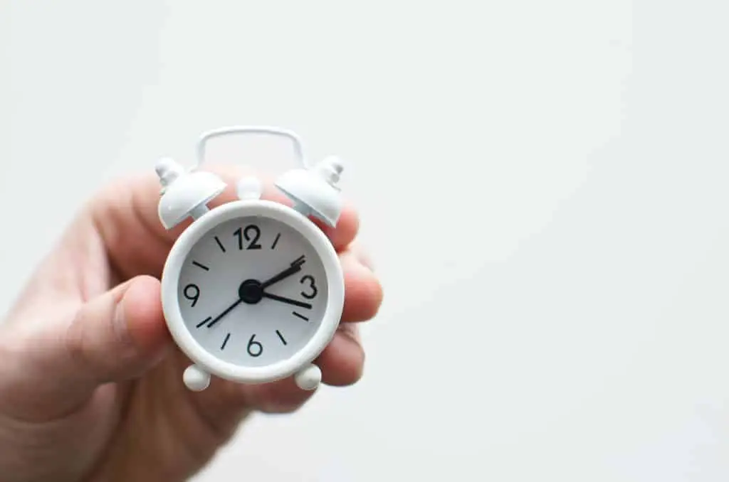 hand holding white alarm clock against white background