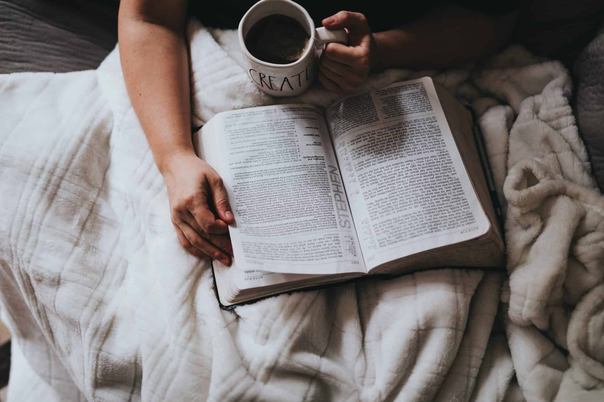 overhead shot of person drinking coffee and reading bible in bed