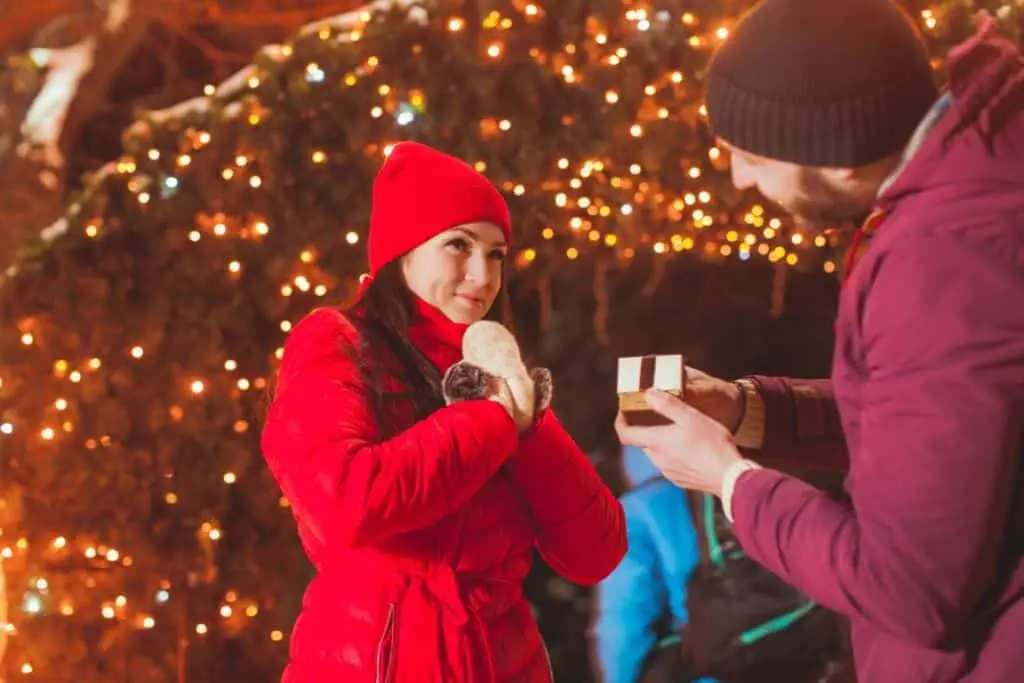 man making a christmas proposal to woman in front of christmas lights