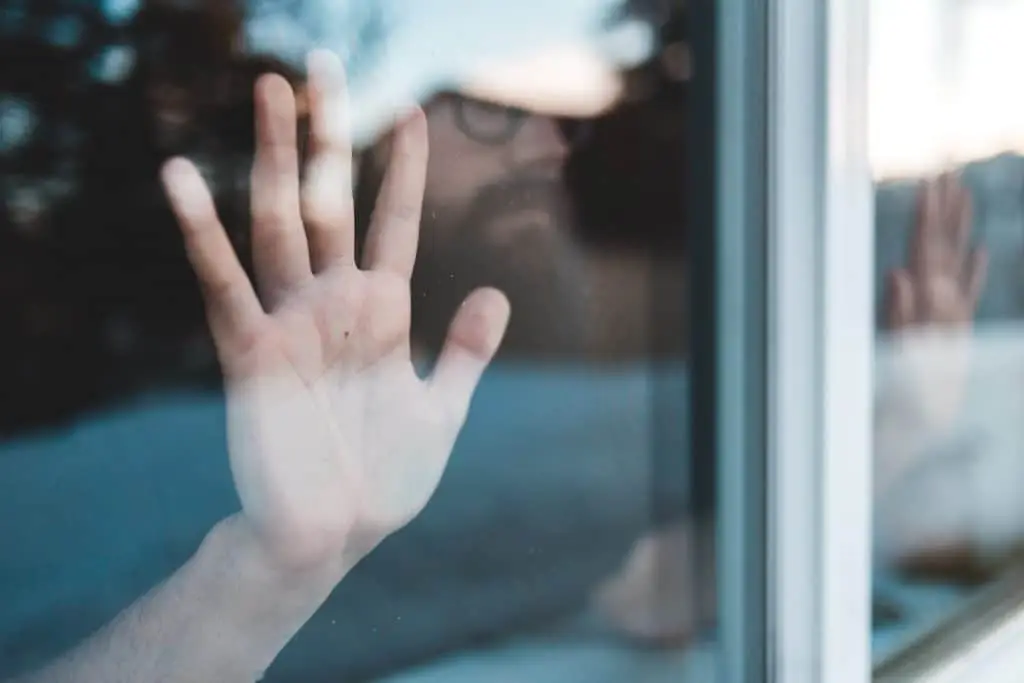 man with hand on window looking outside while in covid quarantine